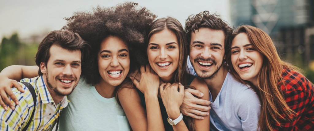 A diverse group of five smiling people standing closely outdoors.
