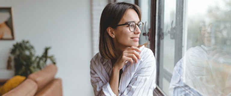Woman smiling and looking out the window in a comfortable office setting.
