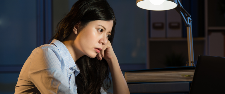 A woman works late at her desk, looking concerned and focused.