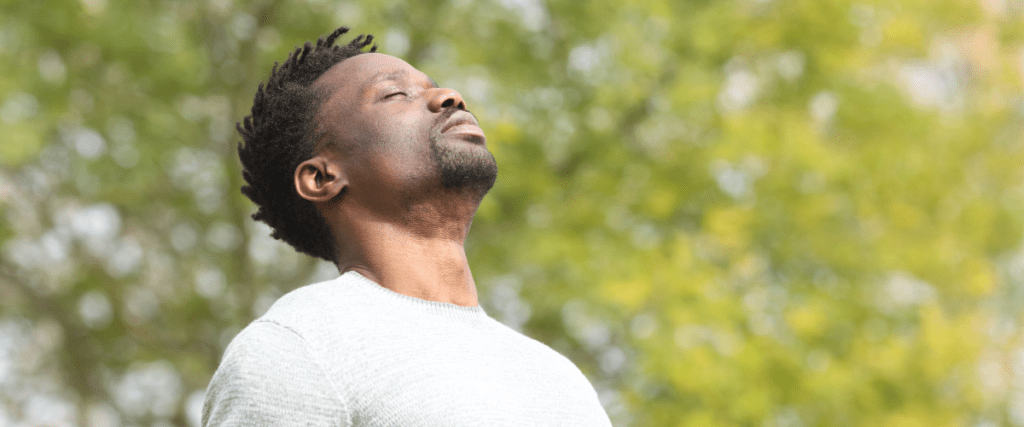 Man enjoying a moment of calm in nature with eyes closed and relaxed expression.