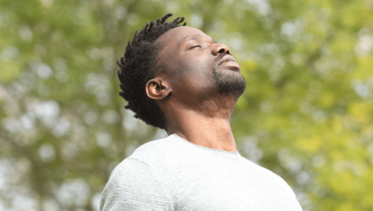 Man enjoying a moment of calm in nature with eyes closed and relaxed expression.
