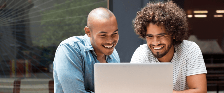 Two colleagues happily collaborating over a laptop in a modern workspace.
